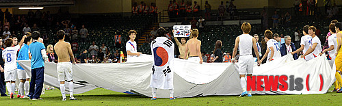 大韓民国が日本に2：0で完勝して銅メダルを確定し、選手たちが大型太極旗を持って「独島（ドクト）は私たちの土地」プラカードを持ち上げて見せている。