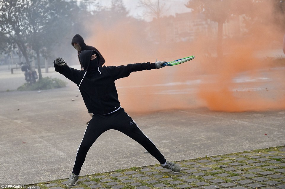 A young man holding a tennis racket throws a projectile at anti-riot police during clashes in Nantes, western France, earlier today