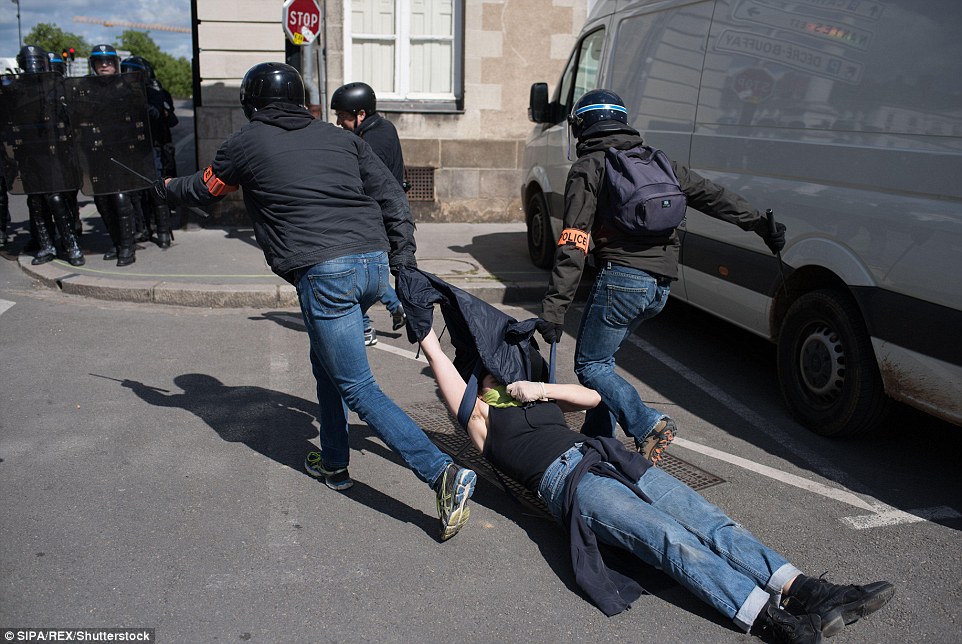 Police officers in riot gear drag a protester along the ground in Nantes, western France, where a car was set alight during a demonstration