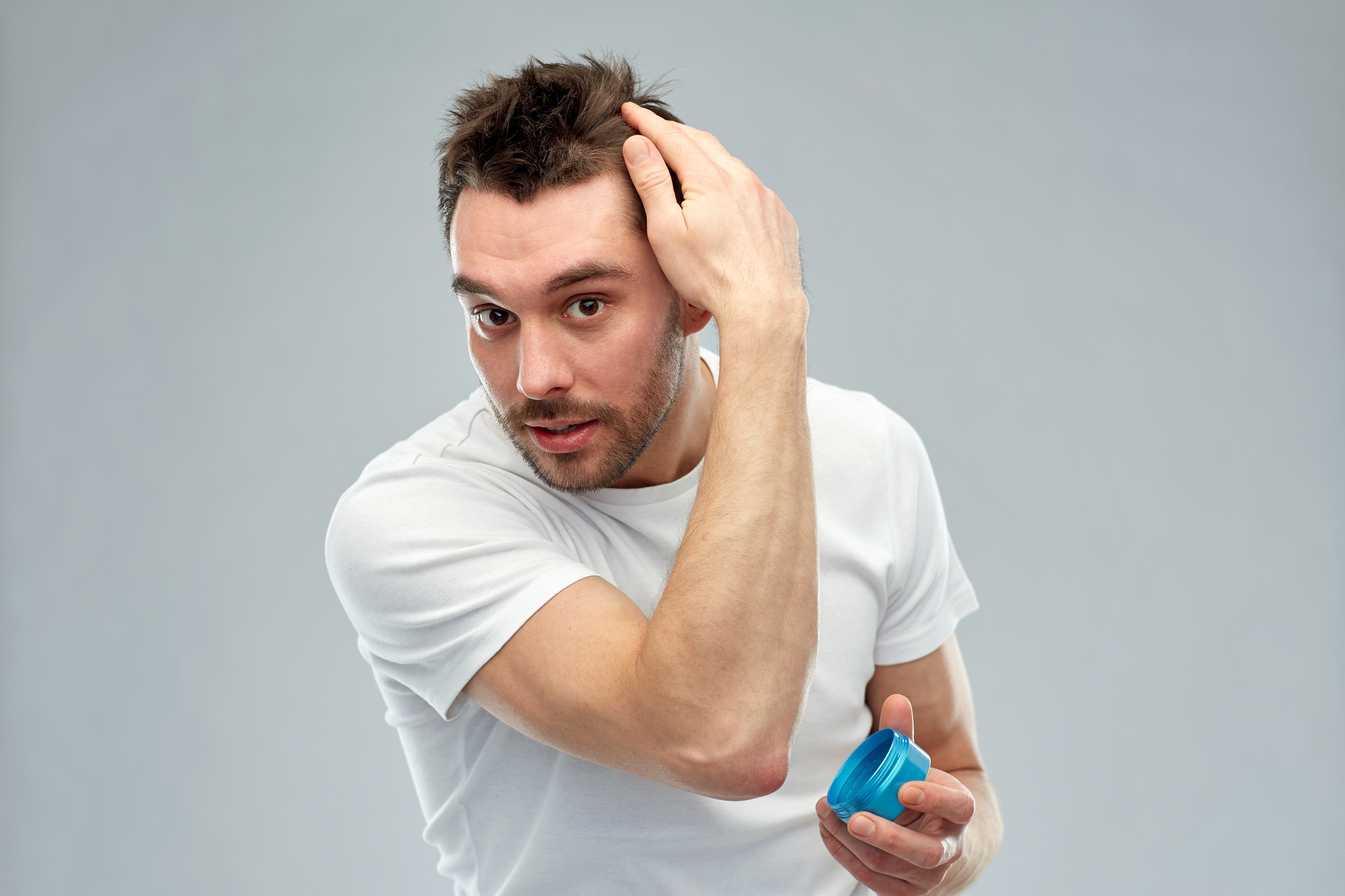 beauty, hairstyle, haircare and people concept - happy young man styling his hair with wax or gel over gray background