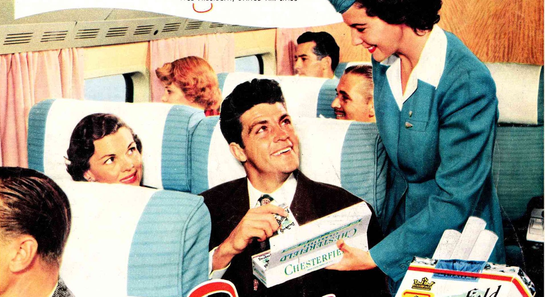 a man sitting in an airplane with a woman serving a box of cigarettes